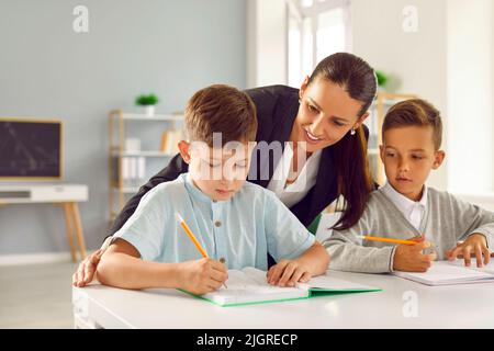 Un professeur amical aide les petits écoliers à effectuer des tests en classe à l'école primaire. Banque D'Images