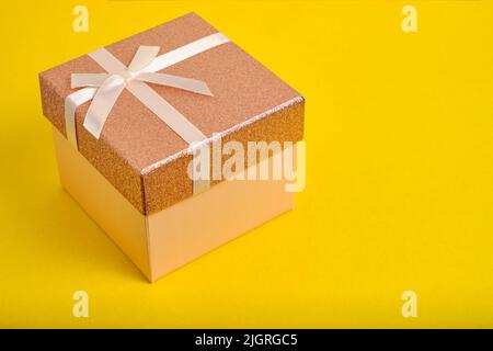 La boîte cadeau beige est ornée d'un ruban et d'un noeud sur fond jaune Banque D'Images