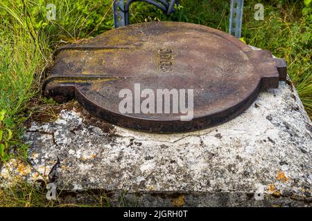 Un couvercle d'égout rouillé repose sur une base en béton à côté du chemin près des ruines de Mirabel, Mirabel-et-Blacons, Drôme, France. Un numéro en relief est fortement érodé et n'est plus clairement lisible. Banque D'Images
