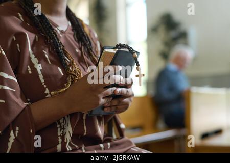 Mains de jeune femme noire avec la Sainte Bible et les perles rosaires avec une petite croix en bois debout dans l'église et priant après le sermon Banque D'Images