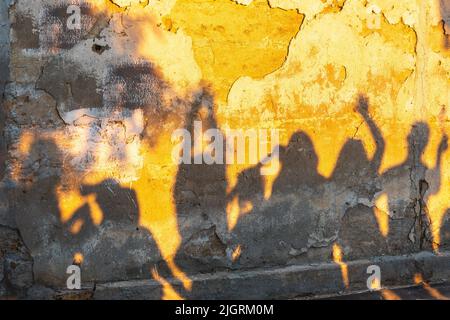 Des ombres de dansant sur un vieux mur au coucher du soleil. Groupe d'ombres humaines sur l'arrière-plan de la paroi en pierre. Banque D'Images