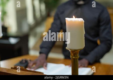 Bougie brûlante blanche sur fond de prêtre lisant les versets de la Sainte Bible tout en se tenant par la chaire et en parlant sermon pendant le service de l'église Banque D'Images