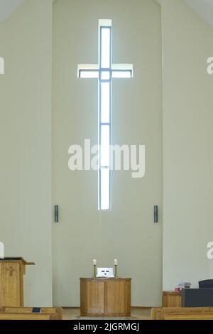 Salle de service vide dans l'église catholique ou évangélique moderne avec croix sur le mur au-dessus de la chaire en bois avec autel et deux bougies Banque D'Images