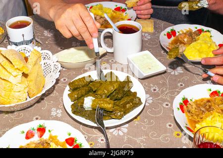 La famille mange à la table du dîner. Dolma sur un plateau, sauce et purée de pommes de terre au chou, mugs avec boissons, vue de dessus. Banque D'Images