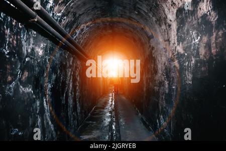 Feu au bout du tunnel souterrain. La silhouette de l'homme entre dans la lumière. Banque D'Images