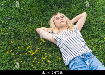 calme paisible jeune fille blonde allongé sur l'herbe en gardant les mains sous sa tête et en rêvant. tir moyen. Photo de haute qualité Banque D'Images