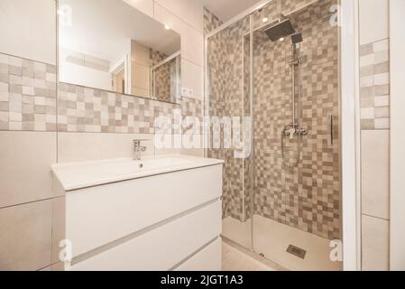 Petite salle de bains moderne avec miroir sans cadre au mur, cabine de douche avec porte coulissante en verre et commode blanche Banque D'Images