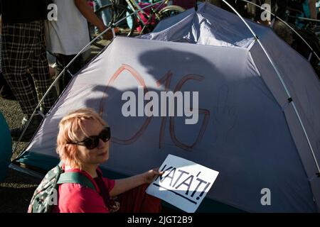 Un manifestant se trouve à côté d'une tente avec un slogan anti-Orban et tient une affiche indiquant « Kata » pendant la manifestation à Budapest. Des centaines de personnes ont protesté contre la modification de la loi sur la taxe Itemized pour les petites entreprises (« KATA » pour le moins en hongrois), Le nouveau projet d'amendement proposé par le gouvernement de Viktor Orban vise à renforcer l'admissibilité à un régime fiscal simplifié auquel de nombreuses petites entreprises ont opté en raison de l'administration allégée et du faible taux d'imposition. Des manifestants bloquent toujours le pont de Margaret sur le Danube, à côté du Parlement. Banque D'Images