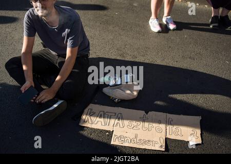 Un manifestant s'assoit à côté de son écriteau tout en bloquant le pont pendant la manifestation à Budapest. Des centaines de personnes ont protesté contre la modification de la loi sur la taxe Itemized pour les petites entreprises (« KATA » pour le moins en hongrois), Le nouveau projet d'amendement proposé par le gouvernement de Viktor Orban vise à renforcer l'admissibilité à un régime fiscal simplifié auquel de nombreuses petites entreprises ont opté en raison de l'administration allégée et du faible taux d'imposition. Des manifestants bloquent toujours le pont de Margaret sur le Danube, à côté du Parlement. Banque D'Images