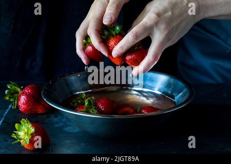 rince les mains de fraises fraîches sur fond sombre. Banque D'Images