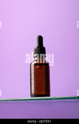 Bouteille de produit cosmétique, verre foncé avec pipette sur étagère en verre, fond violet, regarder vers le haut Banque D'Images
