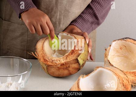 Viande de noix de coco déchiquetée à la main de femme, transformation dans la cuisine Banque D'Images