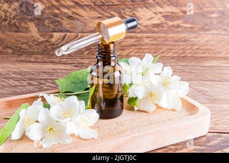 une bouteille ouverte en verre d'huile de jasmin organique se trouve sur un plateau en bois rempli d'huile avec une pipette. fond brun en bois Banque D'Images