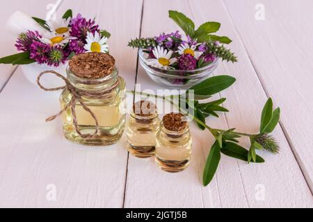 cosmétique naturelle en bouteilles de verre sur une table en bois blanc. fleurs de camomille, trèfle, menthe dans des bols. soin naturel biologique Banque D'Images