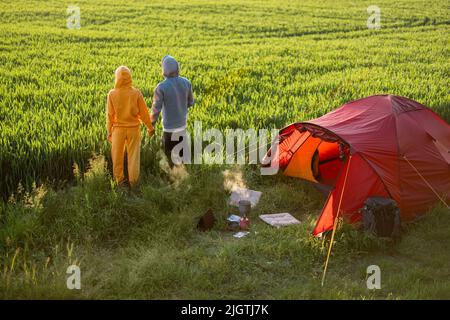 Couple profiter de la vue sur le coucher du soleil au camping sur le terrain vert Banque D'Images