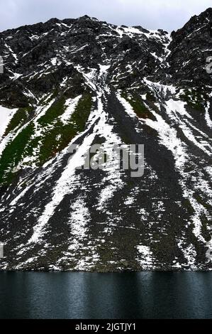 La neige feuilletée se trouve encore en juillet sur les pistes de criques noires dans le canton de Graubunden, en Suisse, au-dessus du Schottensee, un arrêt tranquille sur la route sinueuse des Alpes rhétiennes reliant Davos dans la vallée du Landwasser à Susch dans la Basse-Engadine, Via le col de la Fluela à une altitude de 2 383 m ou 7 818 ft. Banque D'Images