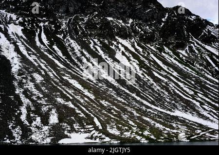 Des stries de neige se trouvent toujours en juillet sur les pentes de criques noires du canton de Graubunden, en Suisse, au-dessus du Schottensee, un lieu tranquille d'arrêt sur la route sinueuse des Alpes rhéotiennes reliant Davos dans la vallée du Landwasser à Susch dans la Basse-Engadine, Via le col de la Fluela à une altitude de 2 383 m ou 7 818 ft. Banque D'Images