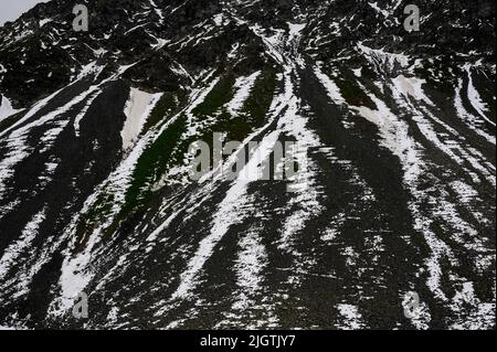 La neige feuilletée se trouve encore en juillet sur les pistes de criques noires dans le canton de Graubunden, en Suisse, au-dessus du lac Schottensee, un arrêt tranquille sur la route sinueuse des Alpes rhétiennes reliant Davos dans la vallée de Landwasser à Susch dans la Basse-Engadine, Via le col de la Fluela à une altitude de 2 383 m ou 7 818 ft. Banque D'Images