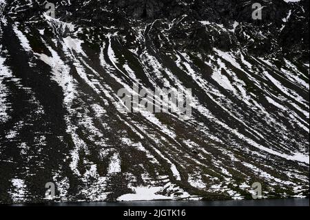 La neige d'été tremblante se trouve encore sur les pistes de criques noires du canton de Graubunden, en Suisse, au-dessus du lac Schottensee, une halte tranquille sur la route sinueuse des Alpes rhétiennes reliant Davos dans la vallée du Landwasser à Susch dans la Basse-Engadine, Via le col de la Fluela à une altitude de 2 383 m ou 7 818 ft. Banque D'Images