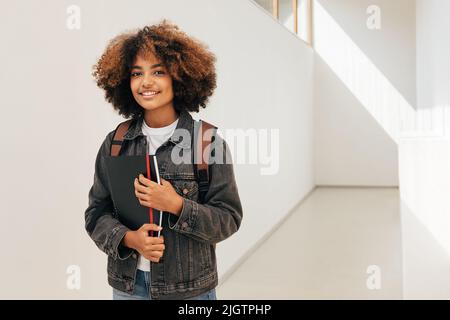 Jeune femme aux cheveux bouclés debout dans le couloir de l'université et regardant la caméra Banque D'Images