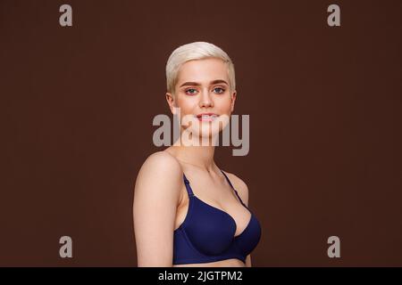 Belle femme blonde avec cheveux courts posant sur fond marron Banque D'Images