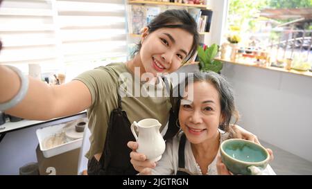 Femme asiatique gaie faisant le selfie avec une femme mature dans un atelier de poterie Banque D'Images