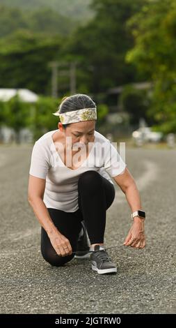 Femme d'âge moyen nouant des lacets, se préparer pour le jogging le matin. Concept de sport et de mode de vie sain Banque D'Images