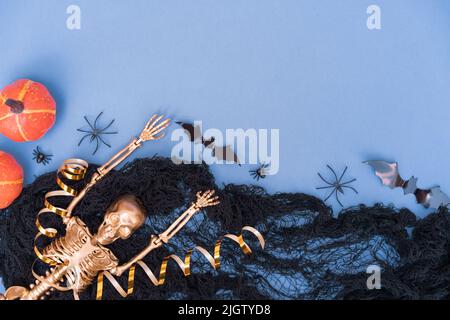 Composition amusante d'halloween avec toile d'araignée noire, araignées, citrouilles, chauves-souris et squelette doré sur bleu avec espace de copie pour le texte. Modèle d'invitation à la fête Banque D'Images