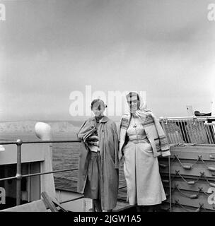 Deux femmes se tiennent sur le pont d'un navire. Derrière eux se trouve une mer et à l'horizon se trouve une plage avec des falaises de craie. Côte sud de l'Angleterre Banque D'Images