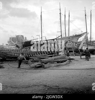 16. Italie. Le journal photo est disponible à B.M.A. + albums photo. Acquisition : livres et documents d'archives. Photos prises 1959-10-28,12 photos en série. Selon les notes: Italie. Côte Adriatique, molfetta, 28/10 -59. Une série de photos des mêmes tours de bateau en bois que les dernières photos sur film 15.A plusieurs coques de bateau sont sur un plan. Deux hommes travaillent avec les coques. Banque D'Images