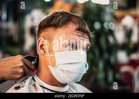 Boutique de photos Lifestyle. Jeune homme le client porte un masque facial, surpris look insatisfait, fronces ridées. Outil de peigne de travail à main pour coiffeur mâle Banque D'Images
