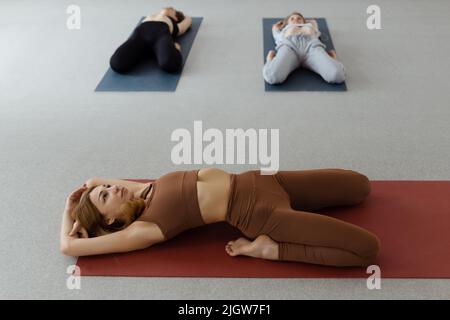 Jeune femme mince couché en Supta Virasana, posture de héros inclinable, étirement des muscles abdominaux et du dos sur le tapis en salle de sport Banque D'Images