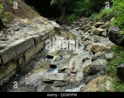 Petit ruisseau boueux au milieu des berges en pierre du parc Banque D'Images