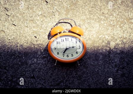 Réveil orange de style vintage sur une surface en béton, sous l'ombre sombre et la lumière vive. Banque D'Images
