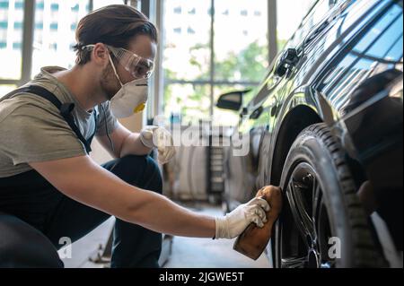 Un employé de la station-service polissage du pneu de la voiture Banque D'Images