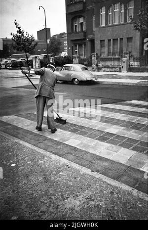 Original-Bildunterschrift: Er Hat sich den Regen von heute morgen zu Nutze gamcht und bringt die Zebrastreifen auf dem Kurfürstendamm mit seinem Schrubbesen auf Hochglanz, Berlin, Allemagne 1955. Banque D'Images