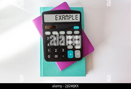 Sur une table blanche se trouve une calculatrice intitulée EXEMPLE. Concept d'entreprise Banque D'Images