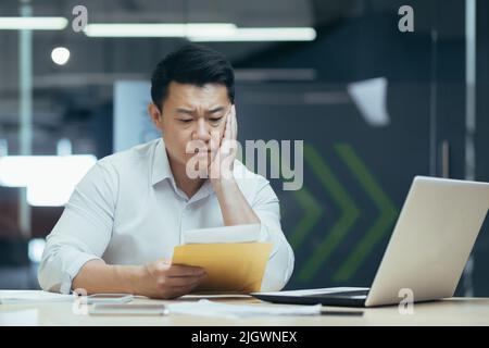 Triste de penser que l'homme d'affaires asiatique a lu de mauvaises nouvelles de la banque, le patron masculin en chemise travaillant dans le bureau Banque D'Images