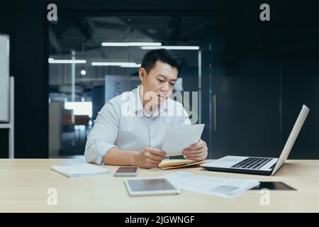 Triste de penser que l'homme d'affaires asiatique a lu de mauvaises nouvelles de la banque, le patron masculin en chemise travaillant dans le bureau Banque D'Images