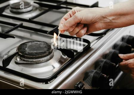 La main d'une femme adulte avec une allumette allume un brûleur à gaz ou un poêle à gaz dans son appartement. Banque D'Images