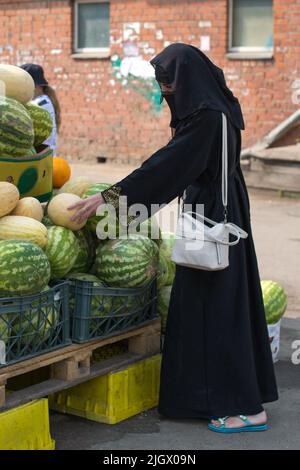 Une femme musulmane vêtue de vêtements nationaux choisissant des pastèques et des melons sur le marché. Banque D'Images