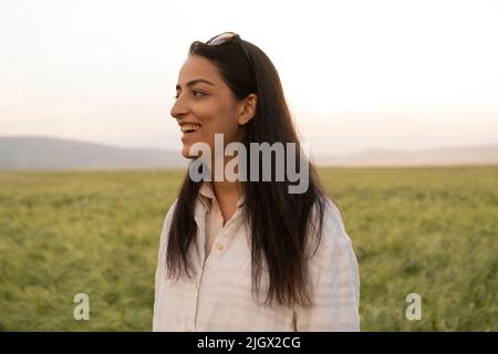 Femme souriante, belle brune aux cheveux longs femme souriante. Debout dans le champ de blé vert. Beau portrait de femme millénaire caucasienne. Banque D'Images