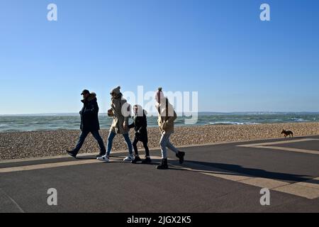 Famille marchant le long d'un front de mer dans le froid avec leur chien suivant sur une certaine distance derrière. Banque D'Images