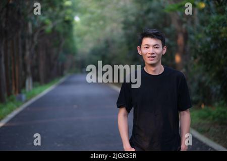 Beau jeune homme asiatique souriant et regardant l'appareil photo dans le parc naturel de la forêt Banque D'Images