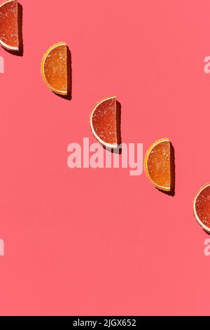 Motif composé de fruits confits colorés orange citron sur fond de corail. Pose à plat. Concept minimal Banque D'Images