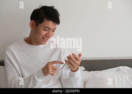 Un jeune homme asiatique souriant utilise et regarde le téléphone à la maison Banque D'Images