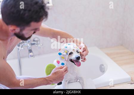 Chien drôle avec bonnet de douche avoir du plaisir avec des bulles de savon dans la salle de bains Banque D'Images