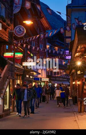 ZERMATT, SUISSE - AVR 11, 2022: Touristes marchant et visitant dans une rue de la ville de Zermatt au coucher du soleil. Banque D'Images