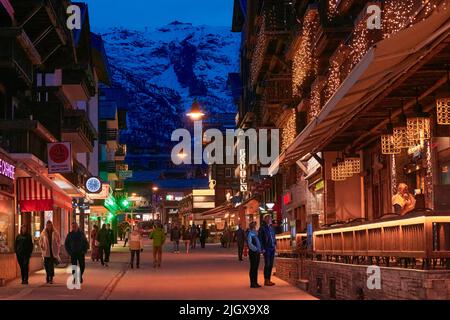 ZERMATT, SUISSE - AVR 11, 2022: Touristes marchant et visitant dans une rue de la ville de Zermatt au coucher du soleil. Banque D'Images