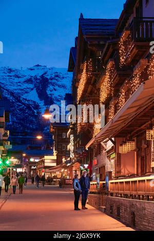 ZERMATT, SUISSE - AVR 11, 2022: Touristes marchant et visitant dans une rue de la ville de Zermatt au coucher du soleil. Banque D'Images